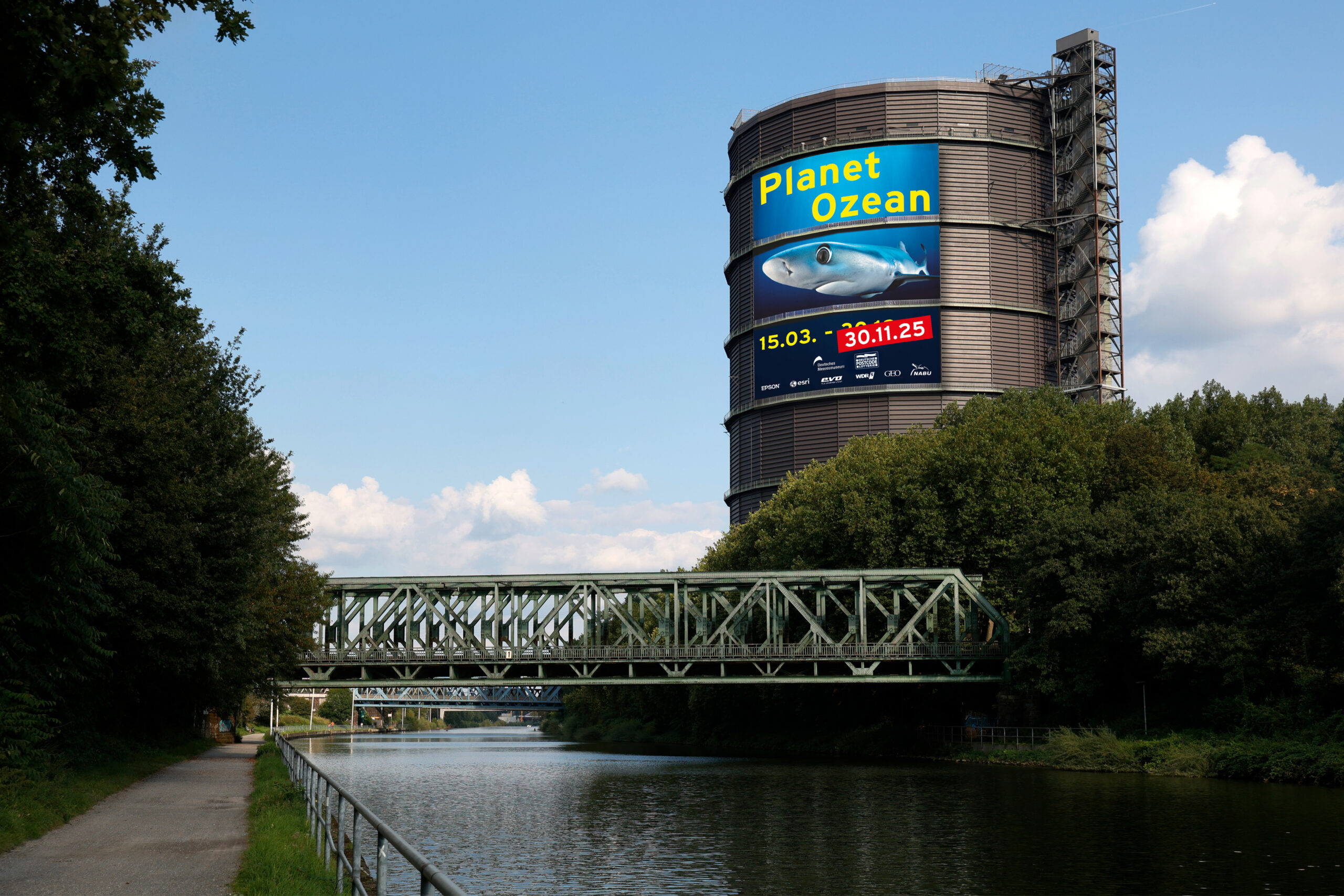 Am Gasometer hängt ein großes Poster 'Planet Ozean' und einem Hai drauf. Im Vordergrund ist eine Brücke und der Rhein-Herne-Kanal.