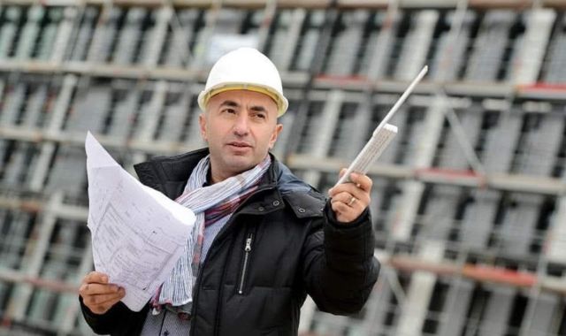 Ein Mann hält einen Zollstock und ein Blätter in der Hand. Er hat einen Helm auf.