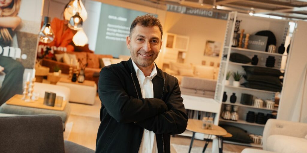 Ein Mann steht im Ausstellungsbereich , hat die Arme verschränkt und lächelt in die Kamera.