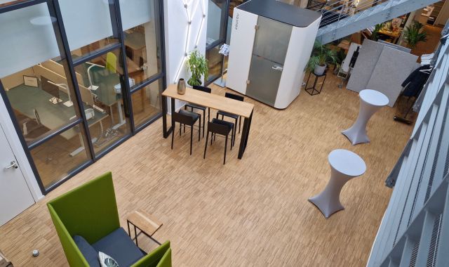 Ein heller großer Raum mt Panoramafenstern, einem Sofa, einem Tisch mit Stühlen, zwei Stehtischen und einer Besprechungsbox.