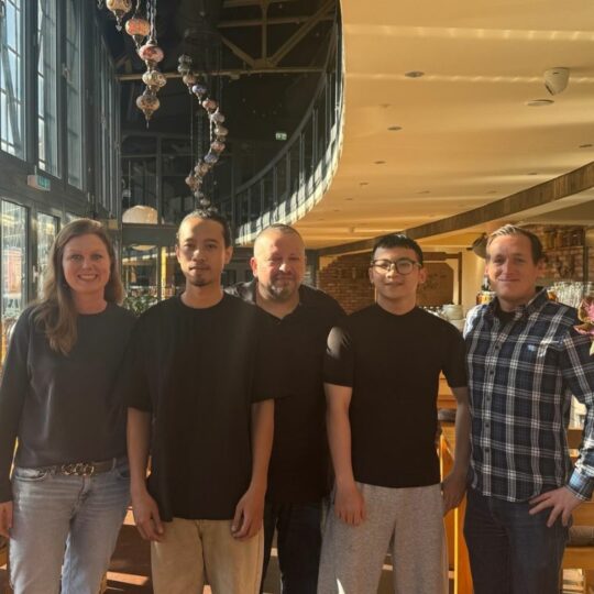 Fünf Personen stehen in einem Lokal nebeneinander und lächeln in die Kamera.