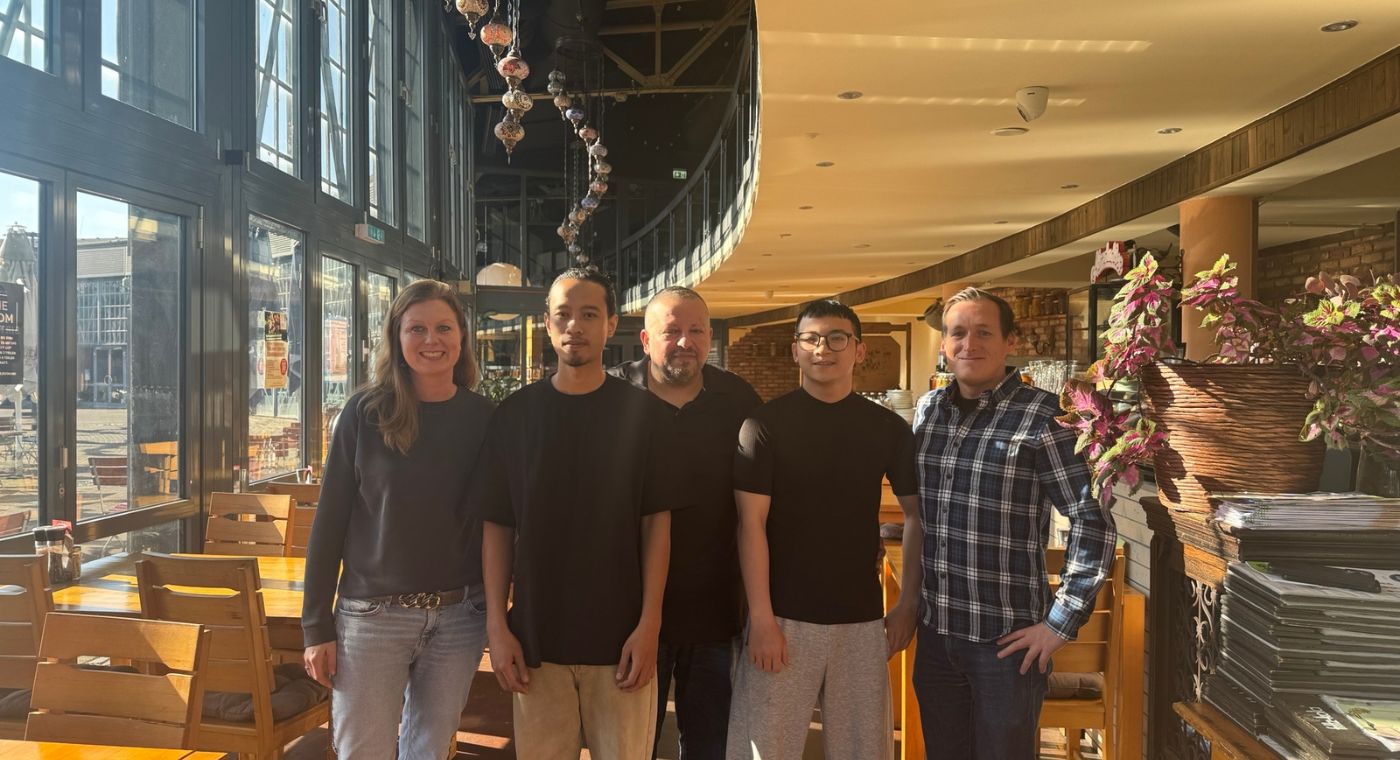 Fünf Personen stehen in einem Lokal nebeneinander und lächeln in die Kamera.