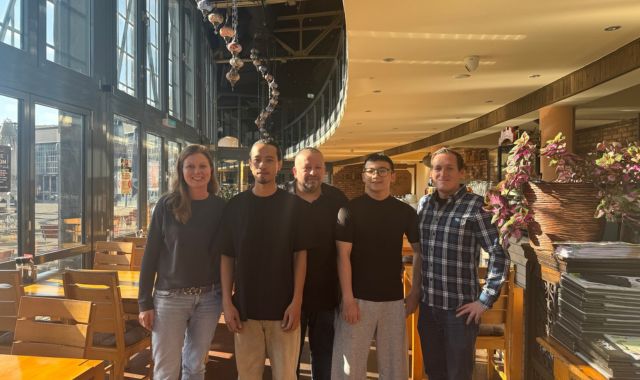 Fünf Personen stehen in einem Lokal nebeneinander und lächeln in die Kamera.