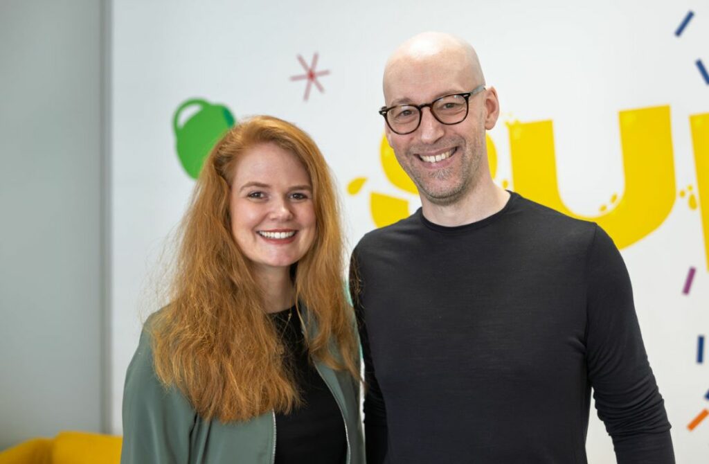 EIne Frau und ein Mann stehen nebeneinander und lachen in die Kamera.