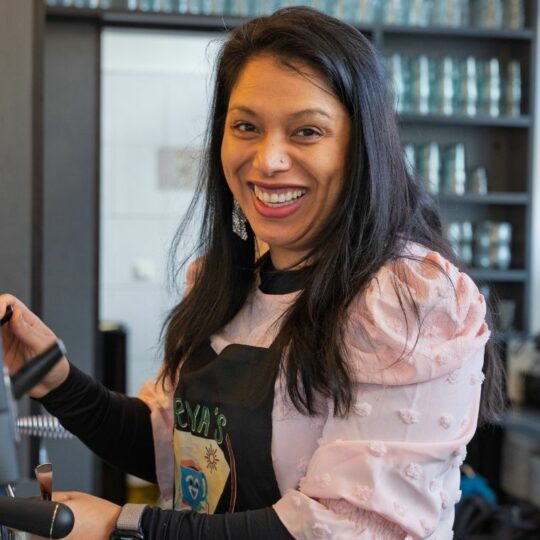 Eine Frau steht an der Kaffeemaschine und lächelt in die Kamera.