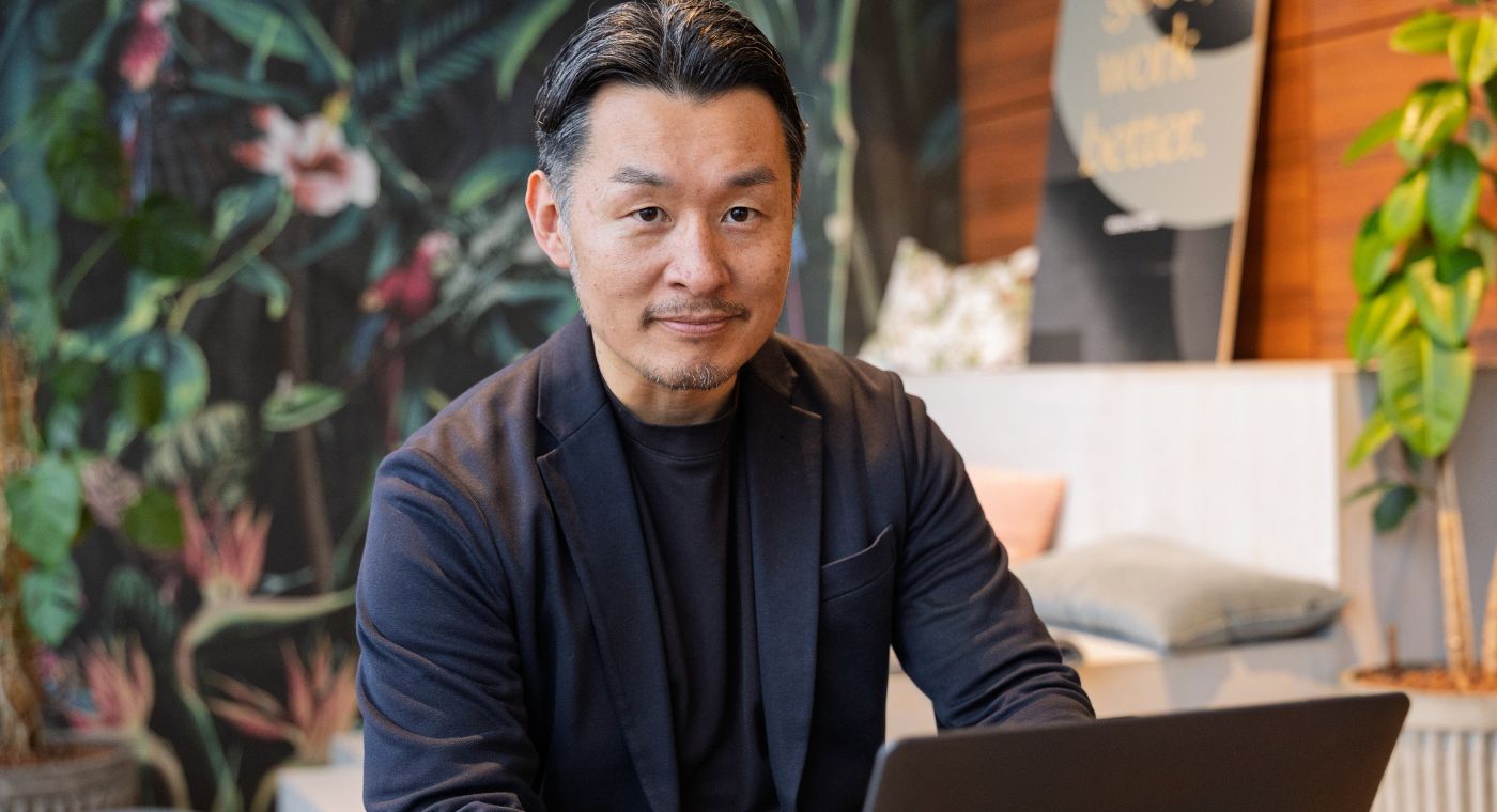 Ein Mann sitzt vor einem Laptop und lächelt in die Kamera.