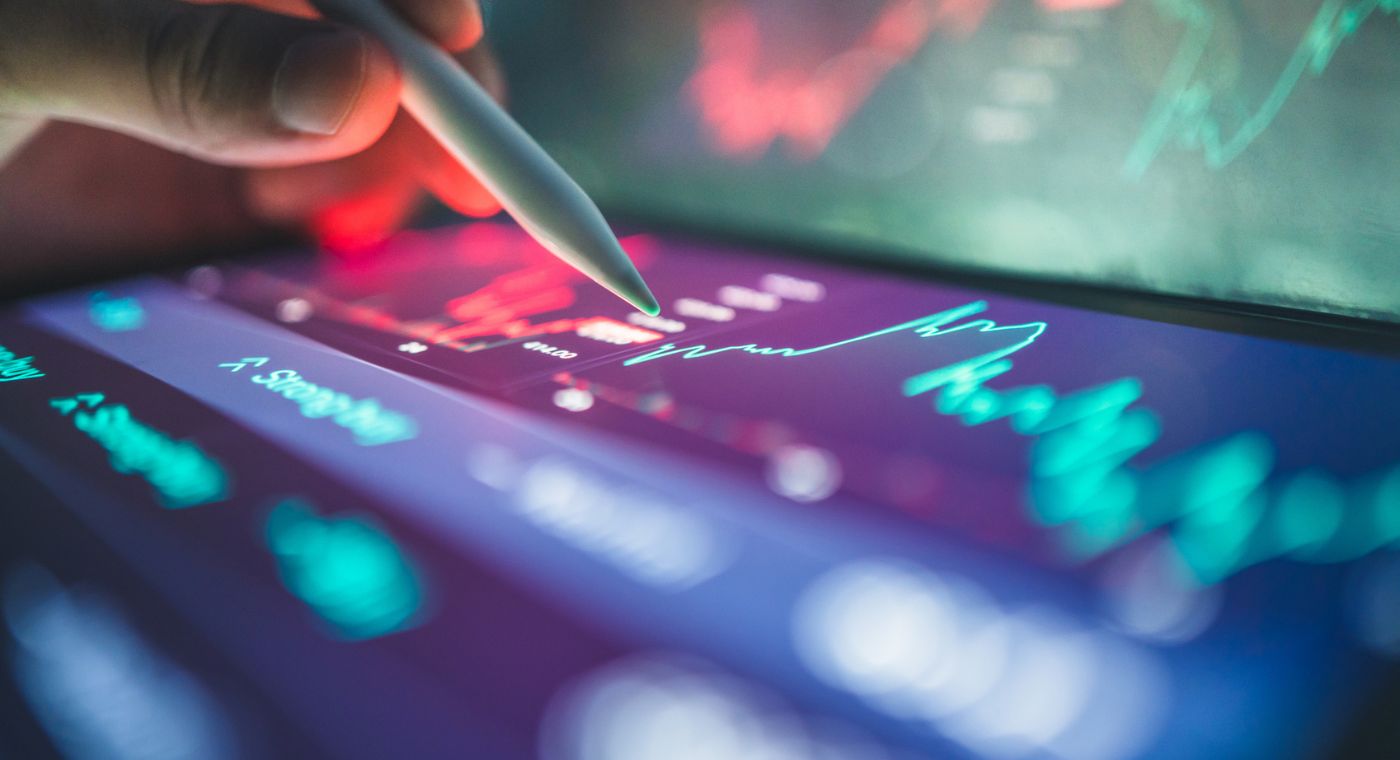 Hand bedient mit einem digitalen Stift ein Tablet, auf dem farbige Diagramme und Finanzdaten angezeigt werden.