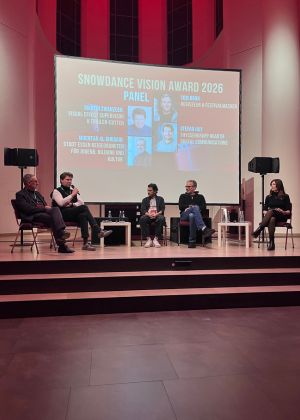 Auf einer kleinen Bühne sitzen fünf Leute auf Stühlen. Im Hintergrund läuft eine Präsentation.