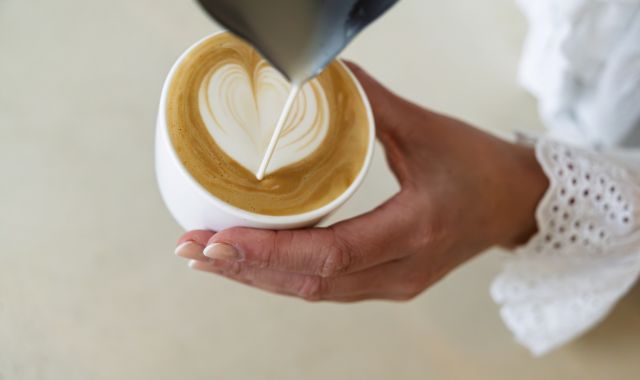 In eine Kaffeetasse wird Milch eingegossen. Im Kaffee ist aus der Milch ein Herzmotiv entstanden.