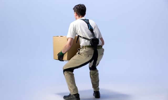 Ein Mann hat ein Exoskelett und hält einen Karton.