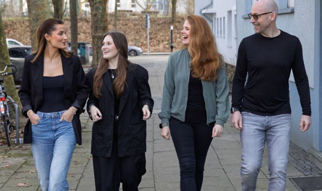Vier Personen laufen auf einem Gehweg, schauen sich an und lachen.