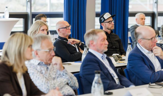 Mehrere Personen sitzen an mehreren Tischen und schauen nach vorne.