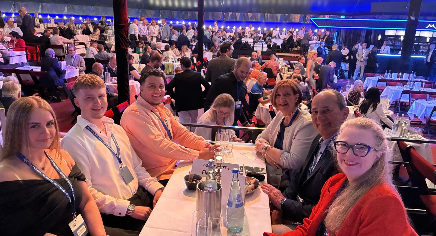 Gruppenfoto von sechs Personen, die an einem Tisch sitzen. Alle lächeln in die Kamera.