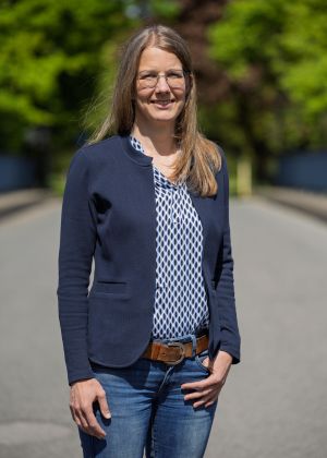 Eine Frau steht in einem Park und lächelt in die Kamera.