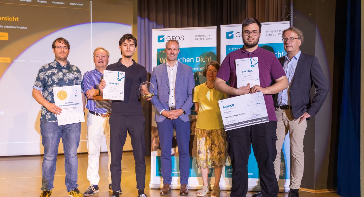 Gruppenfoto von sieben Personen. Sie stehen auf einer Bühne und drei von ihnen halten eine Urkunde in der Hand