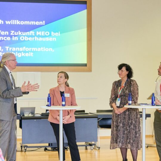 Vier Personen stehen vor einer Präsentation und unterhalten sich.