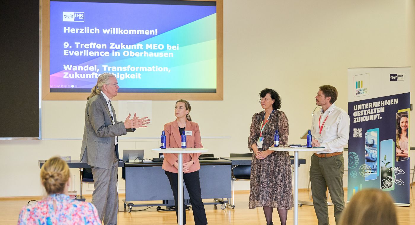 Vier Personen stehen vor einer Präsentation und unterhalten sich.