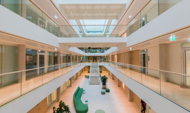 Das Innere eines Gebäudes. Ein großes Treppenhaus mit einem grünen Sofa, vielen Glastüren.