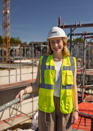 Eine junge Frau steht auf einer Baustelle und lacht in die Kamera