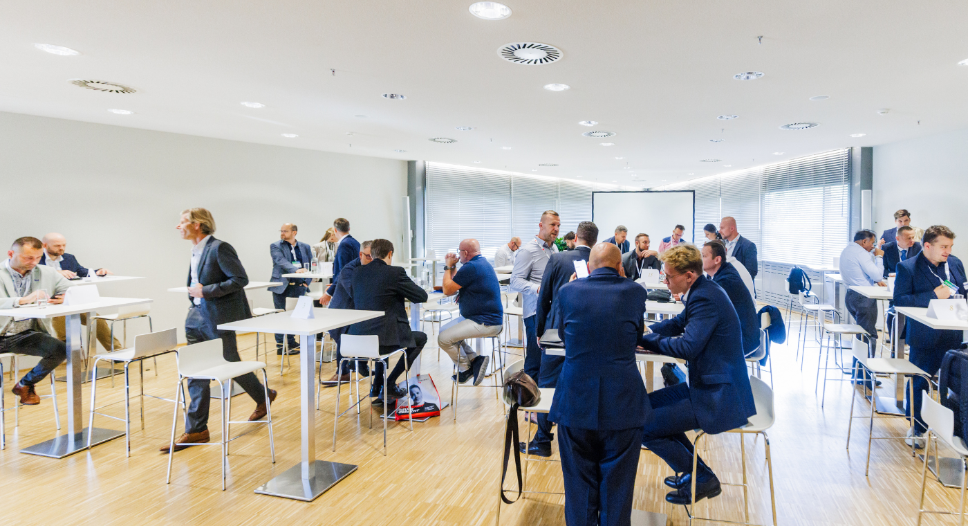 Übersicht des Events. Viele Personen sitzen an Tischen in eine großen Raum und besprechen sich.
